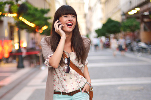 Young woman standing in the city and talking on a mobile phone while laughing.