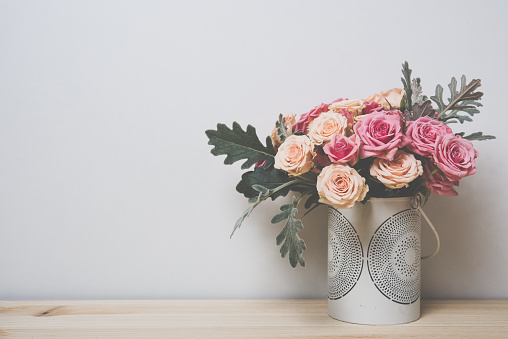 Bouquet of pink and beige roses in a decorative vase on a shelf in home interior, simple home decor