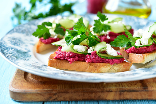 Sandwich with beetroot hummus,cucumber and feta on a vintage plate on blue wooden background.