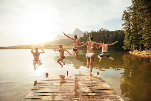 Group of frineds jumping into the lake for a pier. Mid-air, in the water, running, arms in the air...