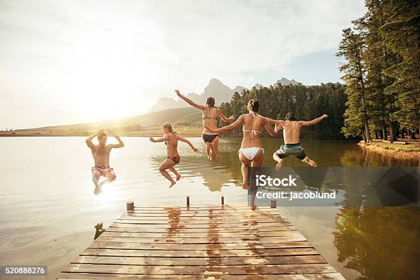Friends Jumping Into The Water From A Jetty Stock Photo - Download Image Now - Lake, Jumping, Summer