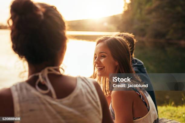 Photo libre de droit de Heureuse Jeune Femme Assise Sur Un Lac Avec Ses Amis banque d'images et plus d'images libres de droit de Amitié