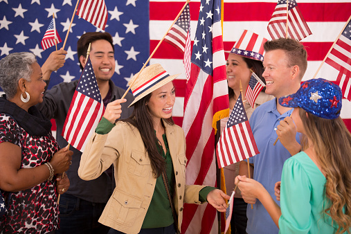 Multi-ethnic and mixed ages group of Americans show excitement during a political rally.  They hold, wave American flags. Primary and presidential elections. Voting concept. 