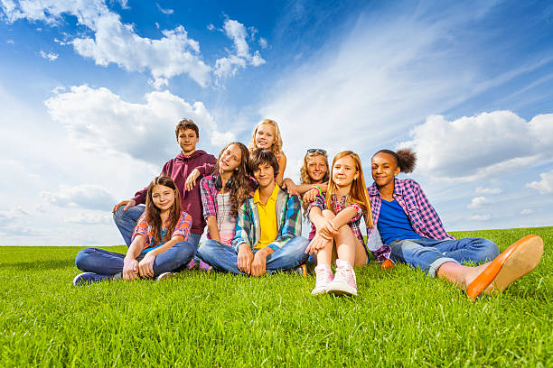 Happy international children sitting together on green meadow during summer sunny day