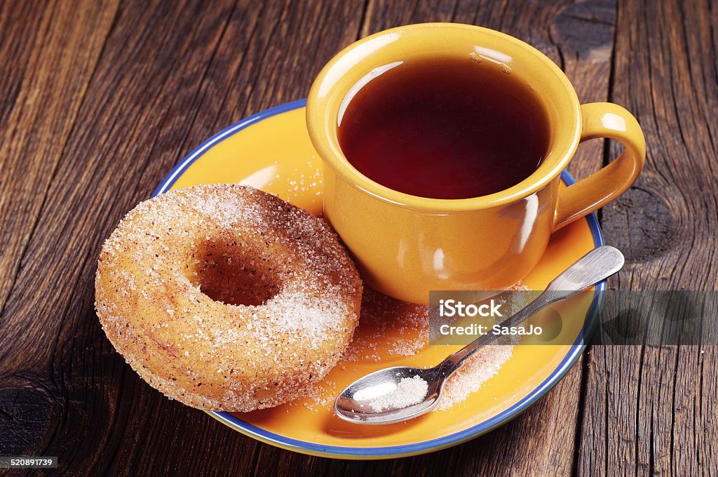 Donut with sugar and tea Donut with sugar and cup of hot tea on wooden table Baked Stock Photo