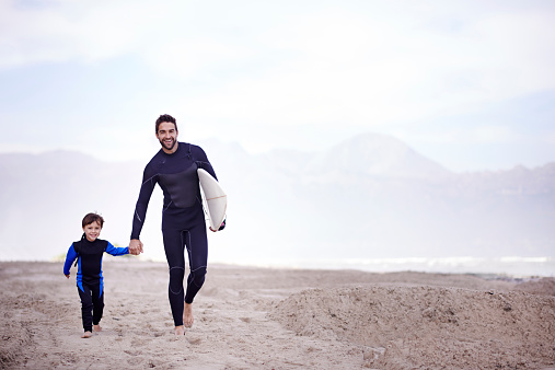 A father walking along the beach with his young son before a surfing lesson