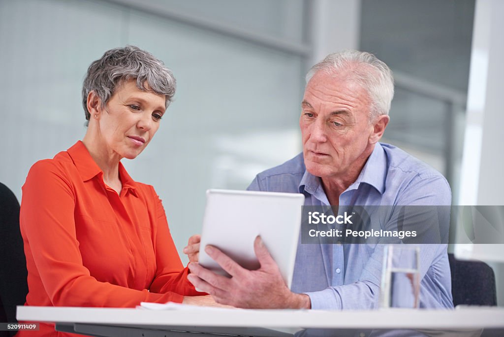 Examining their business plan Shot of two mature business colleagues sitting with a digital tablet and discussing work Adult Stock Photo