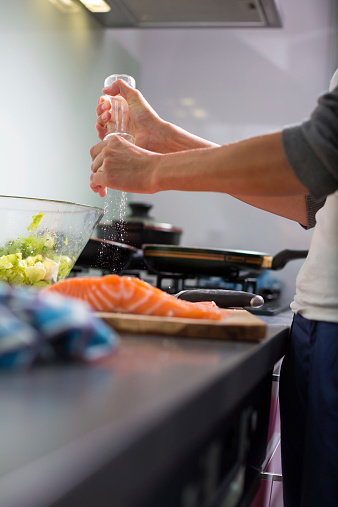 Young woman seasoning a salmon filet in her modern kitchen, prepaaring a healthy food