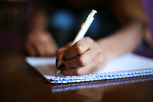 African woman writing in notebook.  Focus on hands.