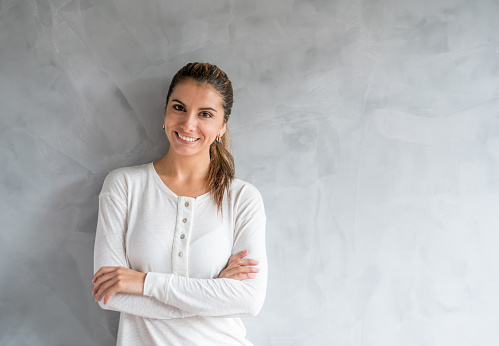 Casual woman looking happy leaning against a marble wall with arms crossed and looking at the camera smiling
