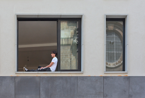 Brussels, Belgium - July 17, 2014: Young man sitting on the window sill of the big house