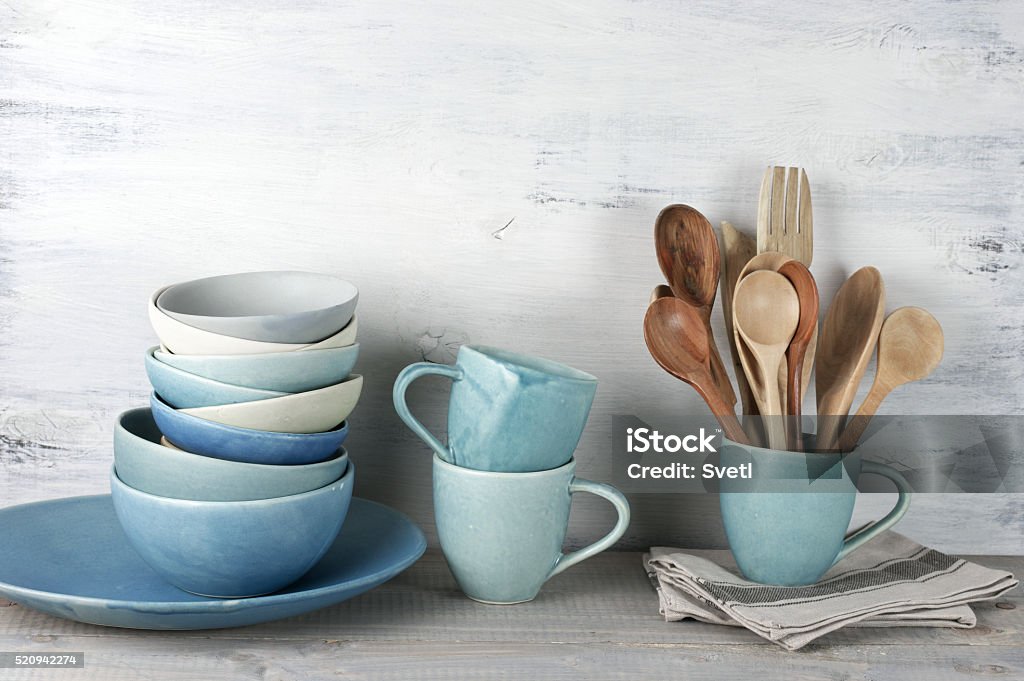 Kitchen utensil set Simple rustic handmade blue crockery against white wooden wall: dish, stack of bowls. mugs and wooden cooking utensils set. Crockery Stock Photo