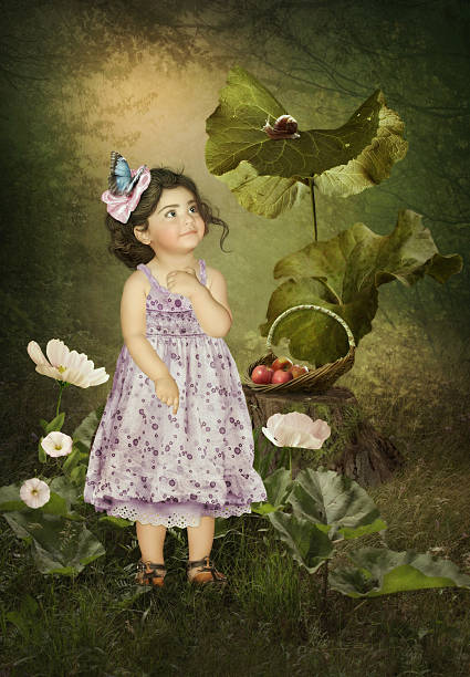 Little girl with a smiling face looking at a snail sitting on a large sheet of burdock in a forest