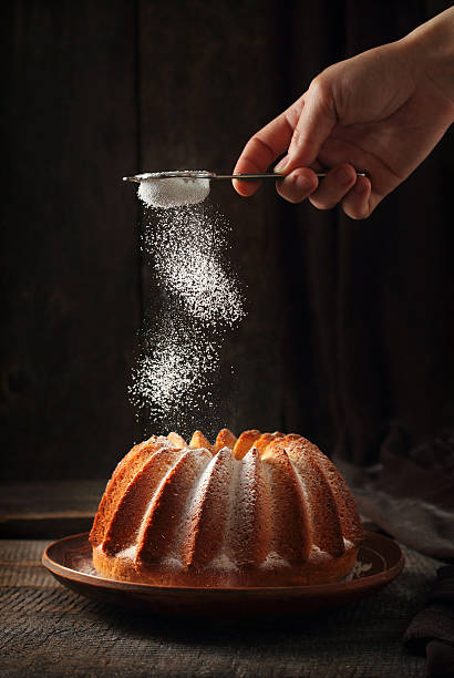 Sprinkling of orange cake with powdered sugar sprinkling of orange cake with powdered sugar, dark wood background, light from one flash and one reflector sprinkling powdered sugar stock pictures, royalty-free photos & images