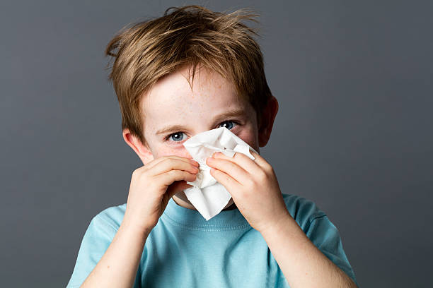 smiling young preschooler with a tissue for cold or rhinitis healthcare learning - smiling young preschooler with red hair and blue eyes using a tissue after a cold or having rhinitis allergies, grey background studio sinusitis photos stock pictures, royalty-free photos & images