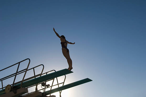 Female swimmer standing on diving board at sunset Female swimmer standing on diving board at sunset diving board stock pictures, royalty-free photos & images