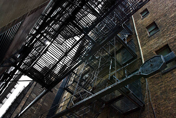 Fire Escape in Dark Alley Alley with old fire escape of a brownstone building. seedy alley stock pictures, royalty-free photos & images