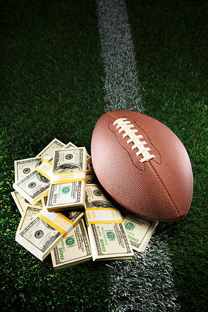 American Football Pile of Cash on Grassy Field This is a photo of an American football next to a pile of cash pertaining to fantasy football, gambling, salaries, etc safety american football player stock pictures, royalty-free photos & images