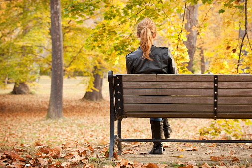 A woman sitting alone in the park enjoying the beautiful fall view.  Lots of room for copy.