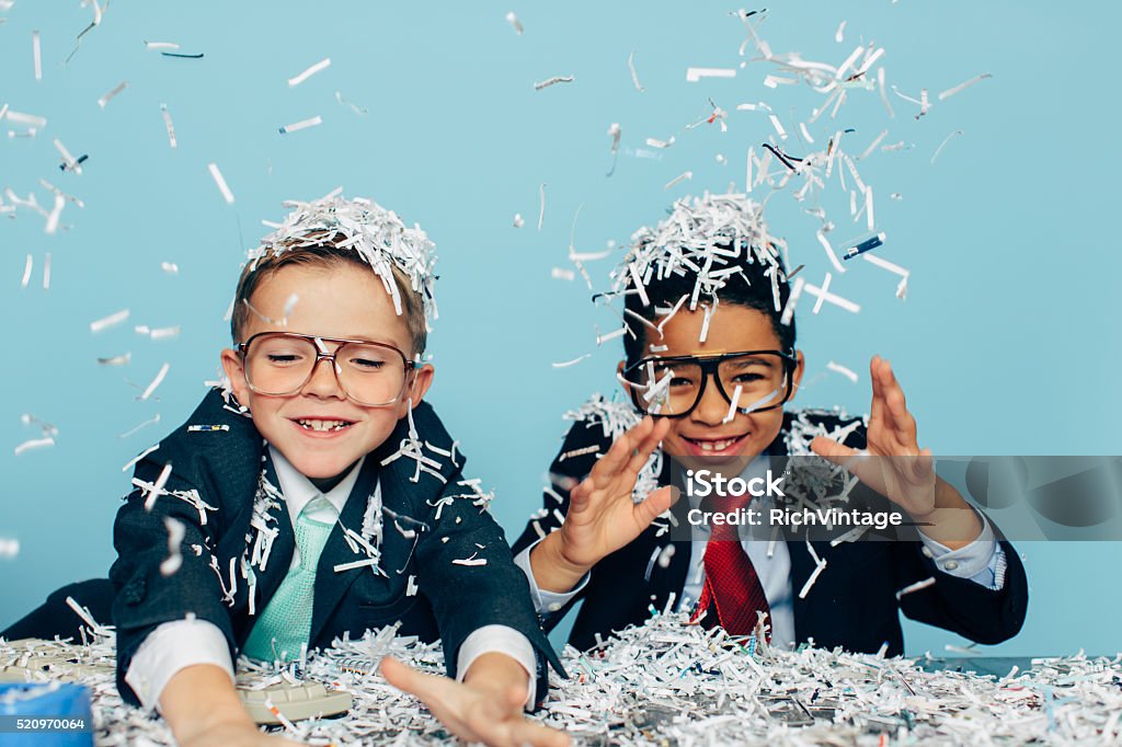 Young Businessmen Partying with Shredded Paper Two young boys and businessman in business attire and glasses sit at an office desk with lots of shredded evidence of their possible business misdeeds. The boys are smiling with as professional work is fun. Or they are throwing an office party. Retro style. Child Stock Photo