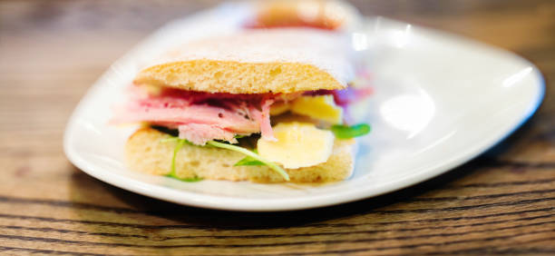 Corned beef sandwich panorama narrow depth of field. The sandwich is made with baguette and sharp cheddar cheese and served on an assymetrical dish.