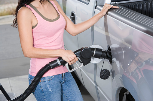 Woman by car with fuel pump, mid section