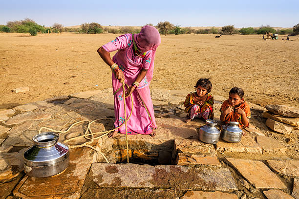 Indian woman drawing water from the well, desert, Rajasthan Indian woman drawing water from the well. Two of her children waiting for her - when she finish drawing water from the well, they together will carry water to the village. Rajasthani women and also children often walk long distances through the desert to bring back jugs of water that they carry on their heads . Thar Desert, Rajasthan. India.http://bem.2be.pl/IS/rajasthan_380.jpg india poverty stock pictures, royalty-free photos & images