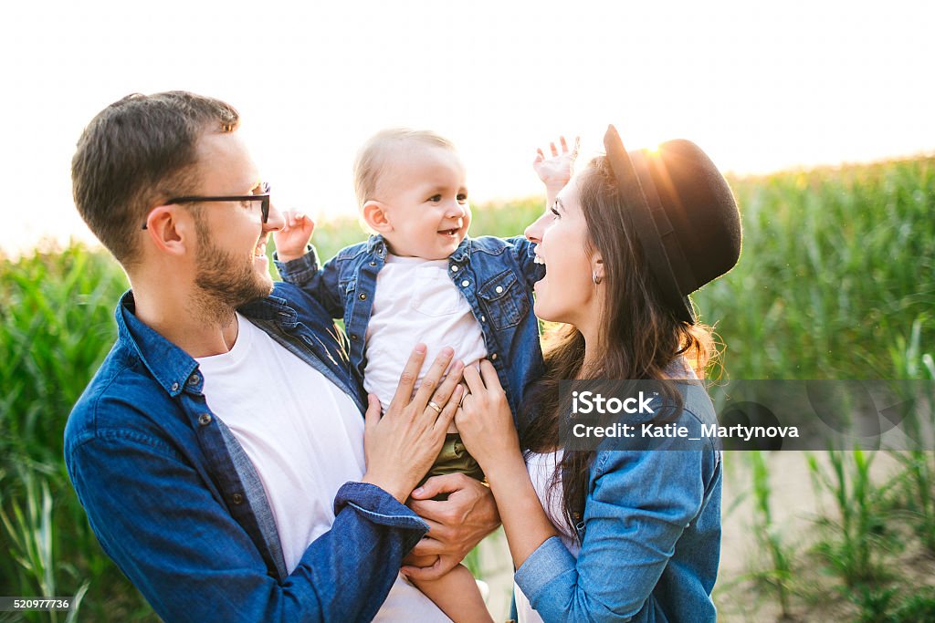 Jovem bonito hipster pai, mãe segurando o bebê no campo de milho - Foto de stock de Família royalty-free