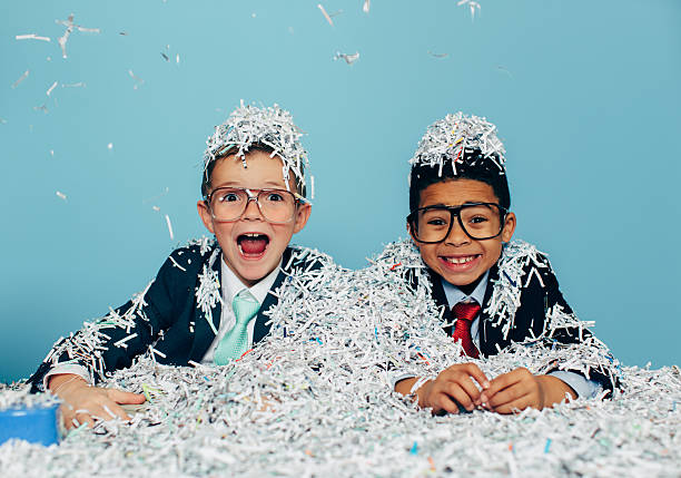 Young Businessmen Partying with Shredded Paper Two young boys and businessman in business attire and glasses sit at an office desk with lots of shredded evidence of their possible business misdeeds. The boys are smiling with as professional work is fun. Or they are throwing an office party. Retro style. shredded stock pictures, royalty-free photos & images