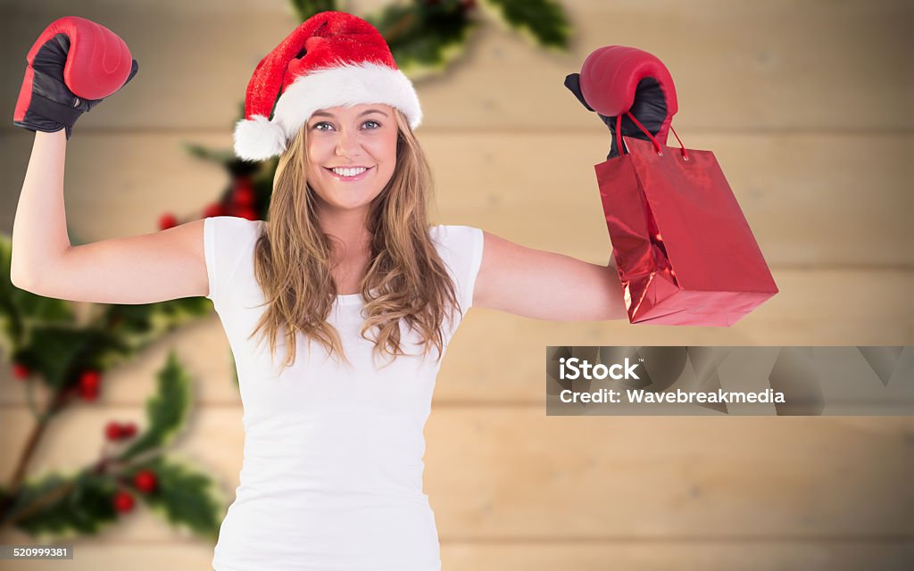 Festive blonde with boxing gloves and shopping bag Festive blonde with boxing gloves and shopping bag against blurred holly on wood 20-24 Years Stock Photo