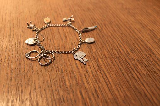 Silver charm bracelet on a scratched wood surface. Selective focus on ring charm and key charm. 