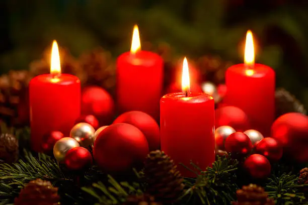 Low-key studio shot of a nice advent wreath with baubles and four burning red candles
