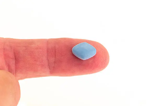 A blue anti-impotence tablet on a patients finger - studio shot with a white background
