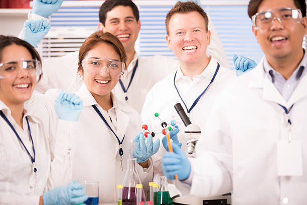 Multi-ethnic group of scientists working inside a research laboratory. Test tubes, beakers, microscope, molecular structure. They are excited about a new discovery they have made during an experiment. 