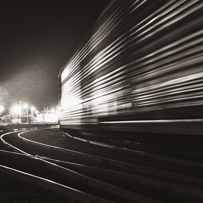 Tall vehicle transport freight cars are shunted towards an Autoport.  Long exposure, toned black and white.