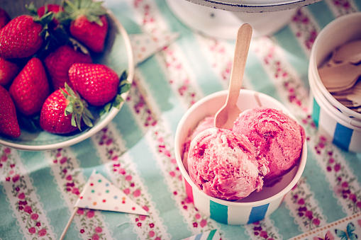 Homemade strawberry ice cream with fresh strawberries in a paper cup. This creamy delicious ice cream is a perfect treat on a sunny day.