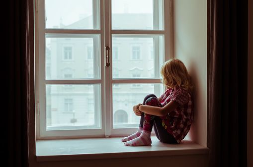 little blond girl sitting and looking over window