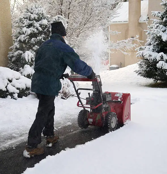 A man uses a snow blower to remove snow from a driveway during a winter storm