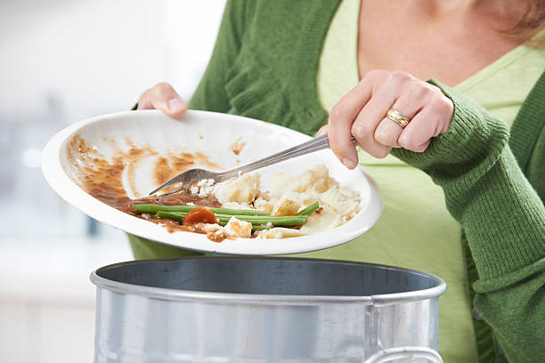 Woman Scraping Food Leftovers Into Garbage Bin stock photo