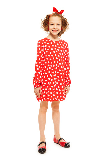 Whole-length portrait of stylish smiling curly-haired girl in red polka-dot dress, isolated on white background