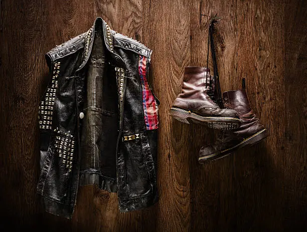 Punk-rock leather jacket and a pair of old boots hanging on a wooden wall