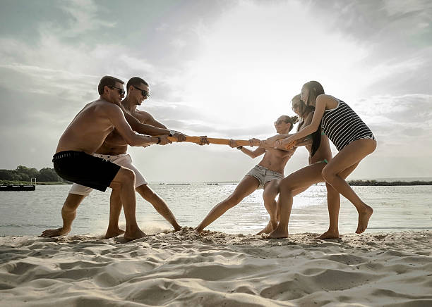 Friends funny tug of war on the beach under sunset sunlight.