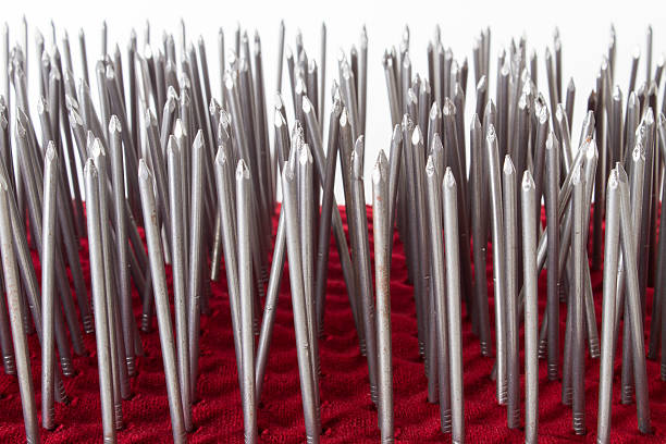 Bed of Nails Pierced red velvet with metal nails in rows on a white background. bed of nails stock pictures, royalty-free photos & images