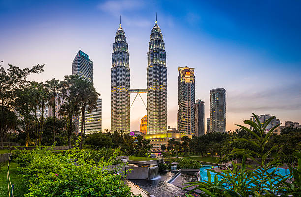 Kuala Lumpur KLCC Park Petronas Towers illuminated at sunset Malaysia The iconic twin spires of the Petronas Towers glittering against the blue dusk sky above the ponds of KLCC Park and Suria KLCC in the heart of Kuala Lumpur, Malaysia's vibrant capital city. ProPhoto RGB profile for maximum color fidelity and gamut. elevated walkway photos stock pictures, royalty-free photos & images