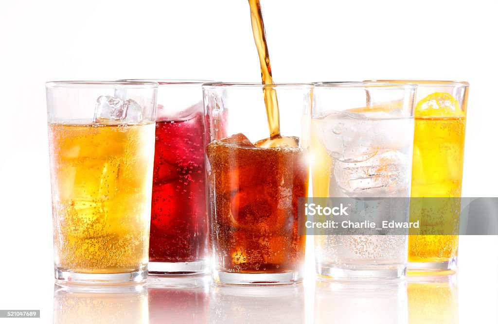 SOFT DRINKS A row of five soft fizzy drinks, with one still being poured.  Drinks are shot with ice and are shot on white reflective background Soda Stock Photo