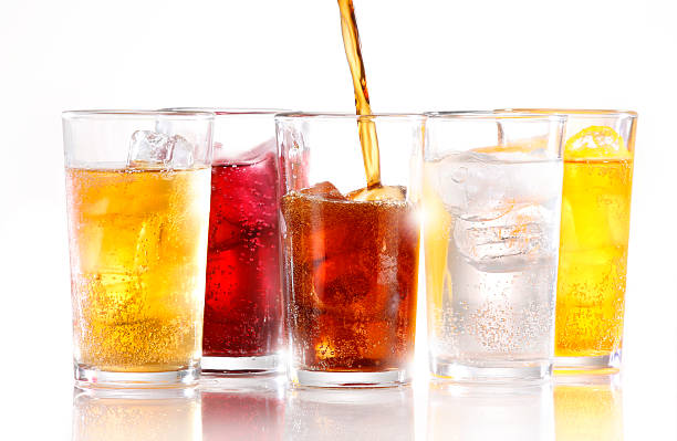 SOFT DRINKS A row of five soft fizzy drinks, with one still being poured.  Drinks are shot with ice and are shot on white reflective background cold drink stock pictures, royalty-free photos & images