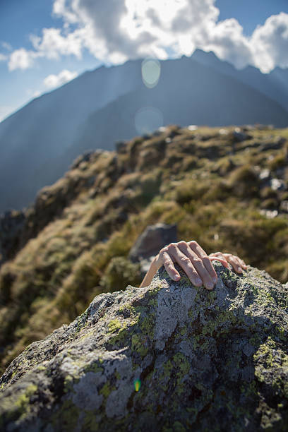istock Human hands grabbing last rock at top of mountain peak. 521048653