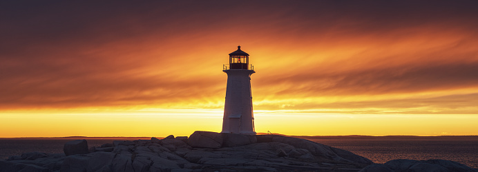 Peggy's Cove Lighthouse is set against a brilliant Spring sunset.  Panoramic view.