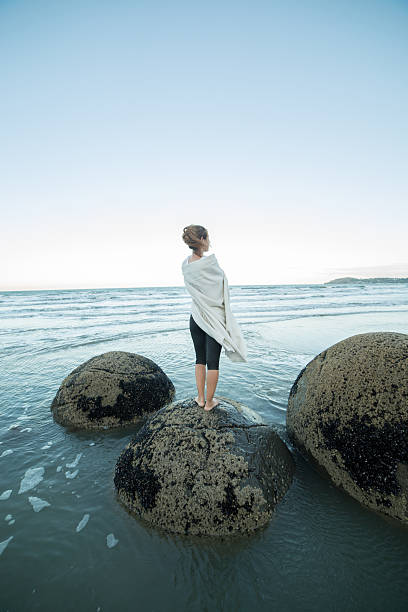 istock Woman wrapped in blanket stands on boulder, looks at view 521087780