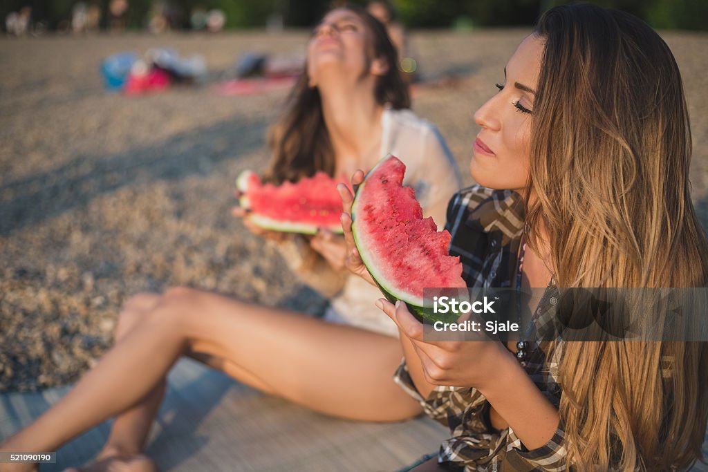 Girlfriends laughing and eating watermelon on the beach Girlfriends laughing and eating watermelon on the beach. Sunset Eating Stock Photo